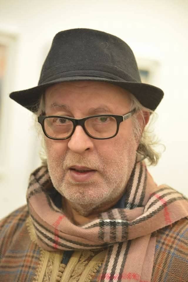 Recent close-up portrait of Omar Sayed, wearing a hat and plaid scarf